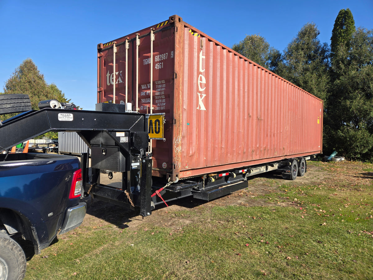Red shipping container attached to a truck on grass with trees in the background